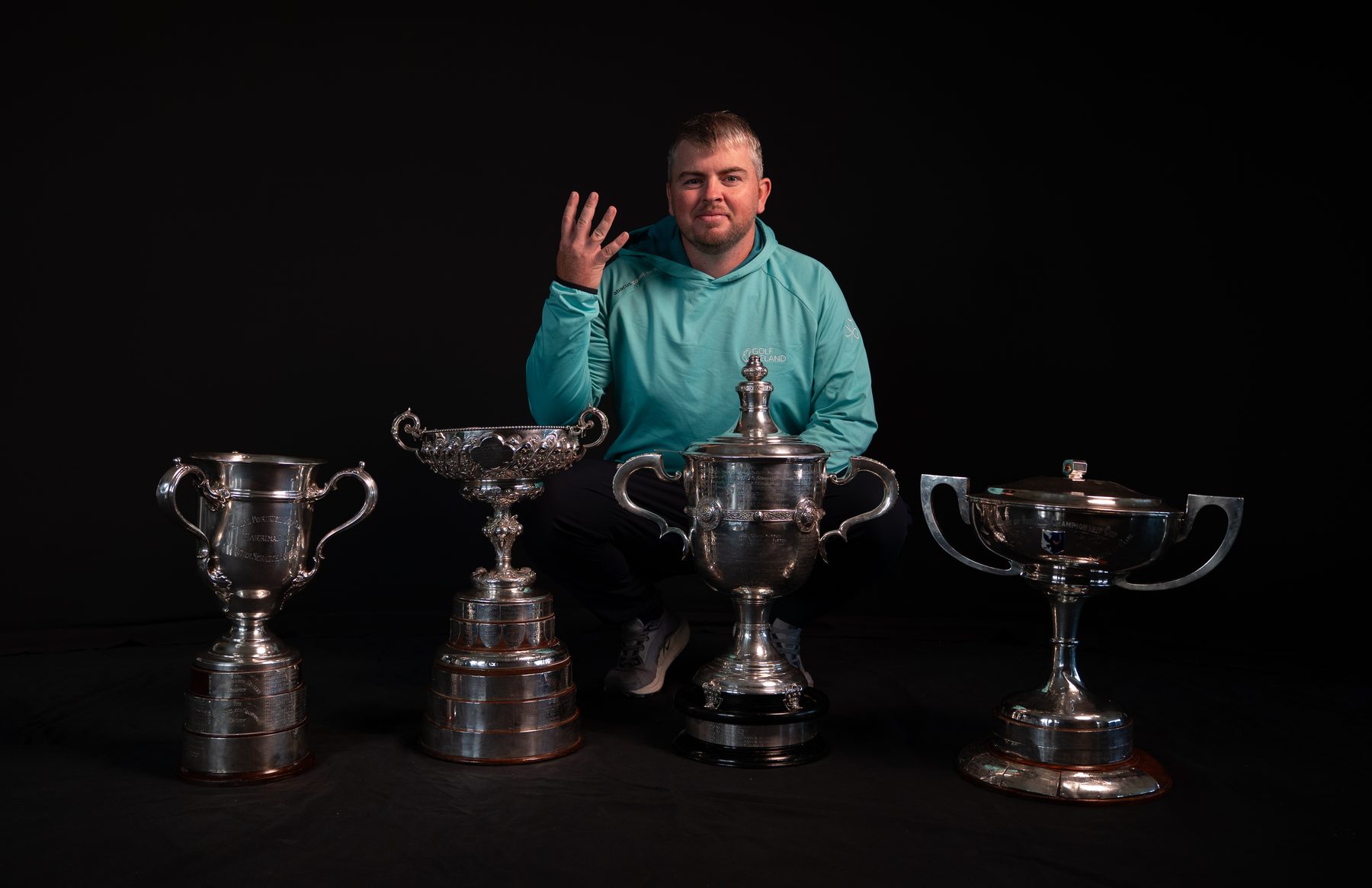 Golfer holding up four fingers behind four trophies, from the Irish Golfer cover shoot
